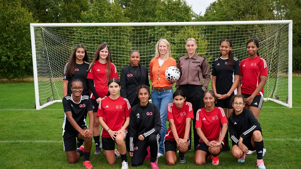 A girls’ football team posing in front of a goalpost on a soccer field, wearing matching black and red uniforms with the 'G3' logo..
